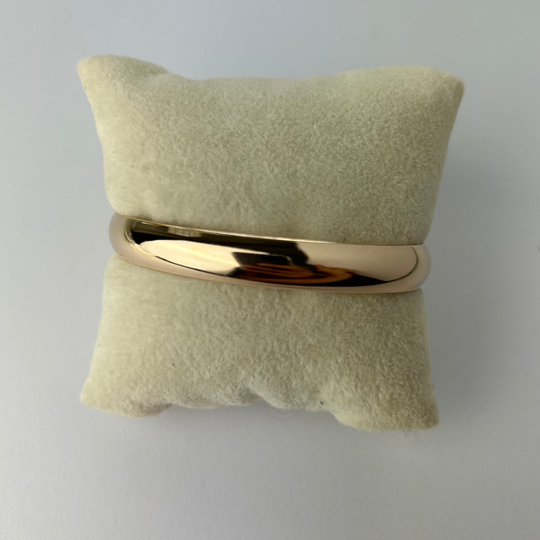 A gold-plated cuff bracelet displayed on a beige textured surface for women