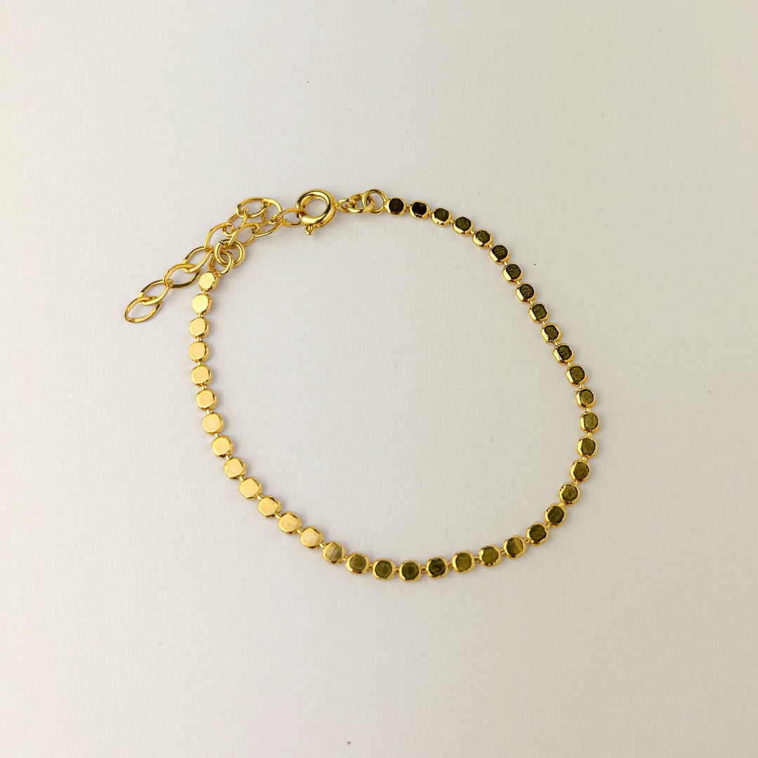 A gold-plated bracelet with small gold beads on a white background