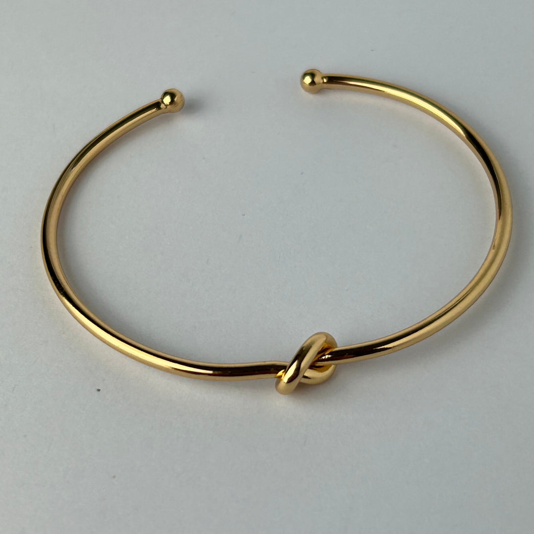 A gold-plated bracelet with a simple, elegant design featuring a central knot for women