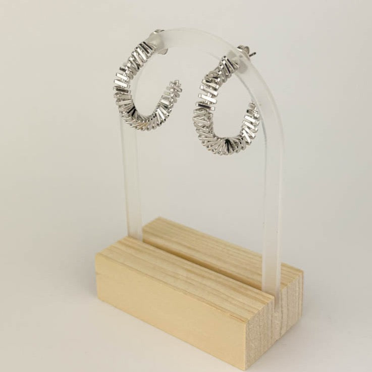 A pair of silver-colored spiral hoop earrings displayed on a clear earring stand with a wooden base.